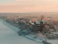 Zimowy krajobraz w Łebie: pokryty śniegiem las i zamarznięte jezioro przy zabytkowym budynku. Łeba atrakcje zimą to widok jak z bajki.