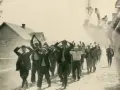 Zatrzymani mężczyźni z rękami w górze na drodze, być może w rejonie granica polsko-niemiecka 1939 Pomorze. W tle domy i żołnierz.