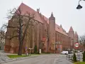 Imponująca katedra w Kwidzynie, z cegły, z charakterystycznymi wieżami i czerwonym dachem, otoczona drzewami i budynkami.