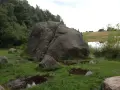 Ogromny głaz, zwany diabelskim kamieniem na Kaszubach, stoi pośród mokrej trawy i kałuż.