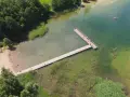 Letnie popołudnie nad jeziorem Hańcza. Ludzie kąpią się i odpoczywają na plaży, inni spacerują po drewnianym pomoście.