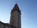 Wysoka wieża z czerwonym dachem, przypominająca dom rybaka, na tle błękitnego nieba.