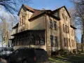 Dawny pałac Poraj, z charakterystyczną werandą i drzewami w tle, otoczony zimowym krajobrazem.