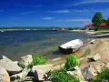 Łódka zacumowana przy brzegu jeziora żarnowieckiego. W tle budynki i zielone wzgórza.