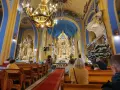 Wnętrze kościoła w Jastarni z wiernymi na ławkach. Złoty ołtarz, błękitne ściany i ozdobny żyrandol tworzą uroczystą atmosferę.