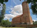 Zamek Człuchów, ceglana wieża i budynek muzeum pod błękitnym niebem z chmurami.