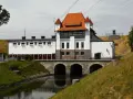Elektrownia wodna Straszyn z charakterystycznym czerwonym dachem i kamiennymi arkadami nad kanałem.