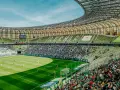 Widok na murawę i trybuny Polsat Plus Arena Gdańsk podczas meczu. Tłumy kibiców na zielonych krzesełkach.