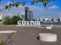 Napis GDYNIA na tle nowoczesnej architektury i żaglowca. Widok na port i budynki w Gdynia old town.