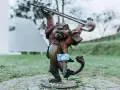 Figurka lew hewelion z kartą miejską w łapie, stojąca na bruku wśród zieleni.