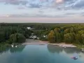 Plaża nad najczystszym jeziorem w Polsce, otoczona lasem. Woda jest turkusowa, na piasku widać ludzi i kampery.