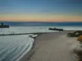 Zachód słońca nad morzem w Gdyni. Na wodzie widać betonową fortecę, a na brzegu piaszczystą plażę i babie doły.