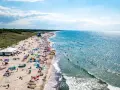 Słoneczna plaża w Darłówku pełna ludzi, kolorowych parawanów i namiotów. Woda w Bałtyku błyszczy, a fale zachęcają do kąpieli. To idealne miejsce na wakacyjne atrakcje.