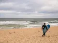 Surfer idzie plażą w Juracie, szukając fal. To jedna z wielu atrakcji tego miejsca.