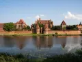 Potężny zamek w Malborku rozciąga się wzdłuż rzeki, jego ceglana powierzchnia lśni w słońcu.