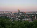 Widok na miasto o zachodzie słońca. W oddali widać nowoczesne budynki, a bliżej dachy domów i zieleń. Jakby pachołek oliwa na tle nieba.