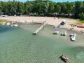 Letnia przygoda na wodzie, kolorowe rowerki wodne i kajaki czekają przy brzegu. Widok na plażę z namiotami i lasem, idealne miejsce na wypoczynek nad jeziorem Binduga 69.