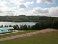 Widok na jezioro i lasy, z basenem pod nowoczesnym zadaszeniem. W oddali majaczy złota góra.