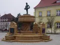 Kamienna fontanna z rzeźbą rybaka na szczycie, ozdobiona płaskorzeźbami statków.