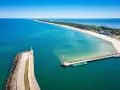 Władysławowo miasto, port z falochronem i latarnią morską, na tle piaszczystej plaży i turkusowego morza.
