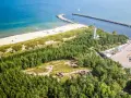 Widok z lotu ptaka na wybrzeże z piaszczystą plażą, lasem i portem. Wśród drzew widoczne są historyczne bunkry nad morzem.