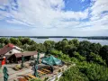 Malowniczy widok na park krajobrazowy pojezierza iławskiego. Taras z zielonymi parasolami i ławkami, jezioro z żaglówką w tle.