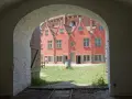 Przez łuk widać dziedziniec twierdzy Wisłoujście z ceglanymi budynkami i zieloną trawą.