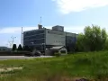 Budynek elektrowni wodnej Żarnowiec z charakterystycznym logo. W tle wieża transmisyjna i zieleń.