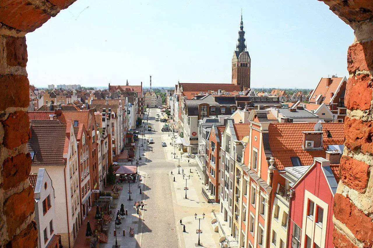 Widok na ulicę w Starym Mieście Elbląg z charakterystyczną wieżą kościelną i kolorowymi kamienicami.