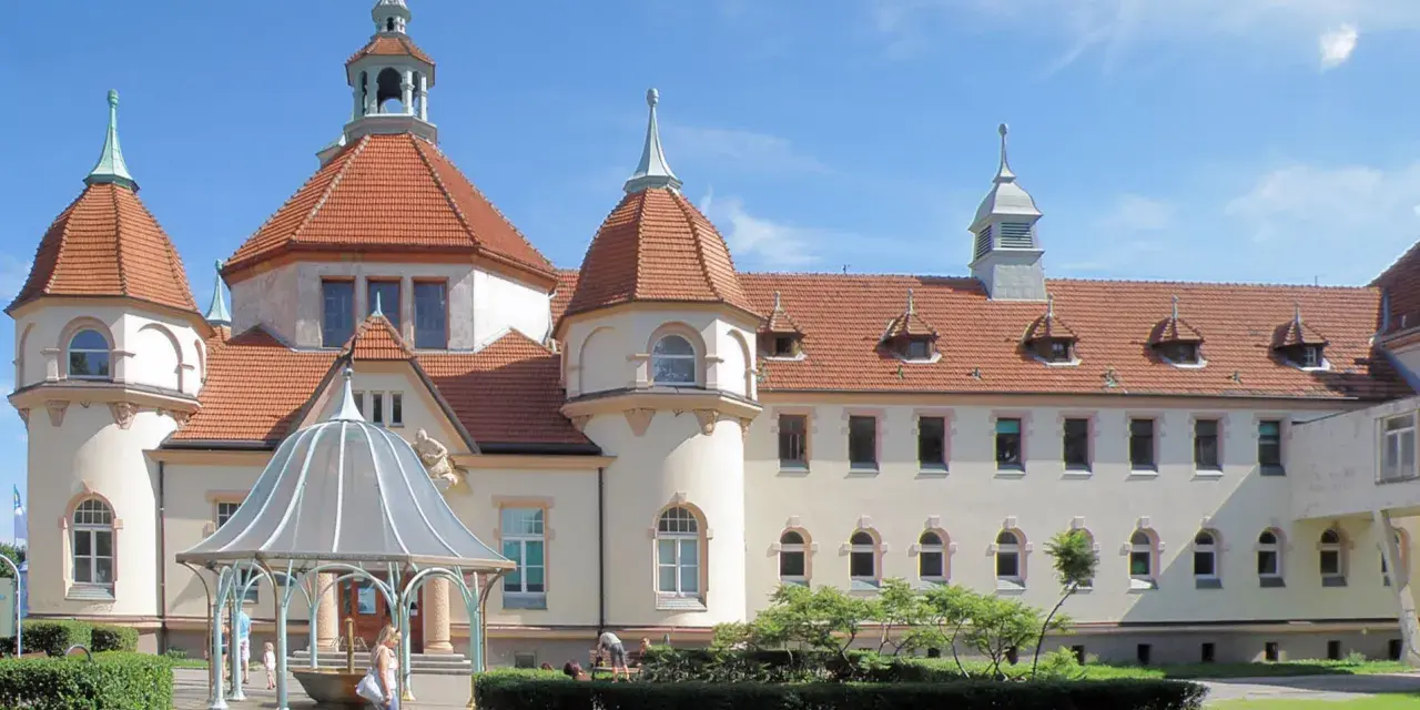 Elegancki zakład balneologiczny Sopot z charakterystycznymi wieżyczkami i czerwonym dachem, otoczony zielenią.