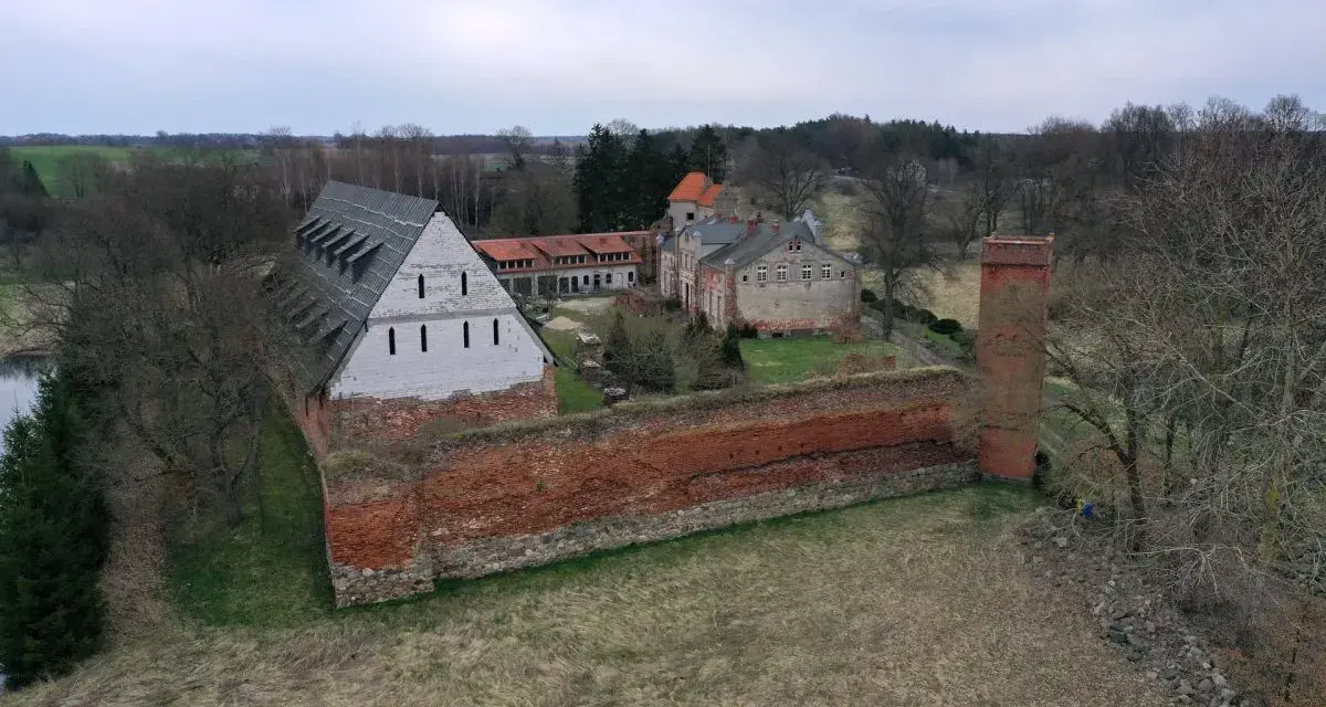 Zamek Kiszewski, z ceglanymi murami i wieżą, otoczony zielenią i drzewami.