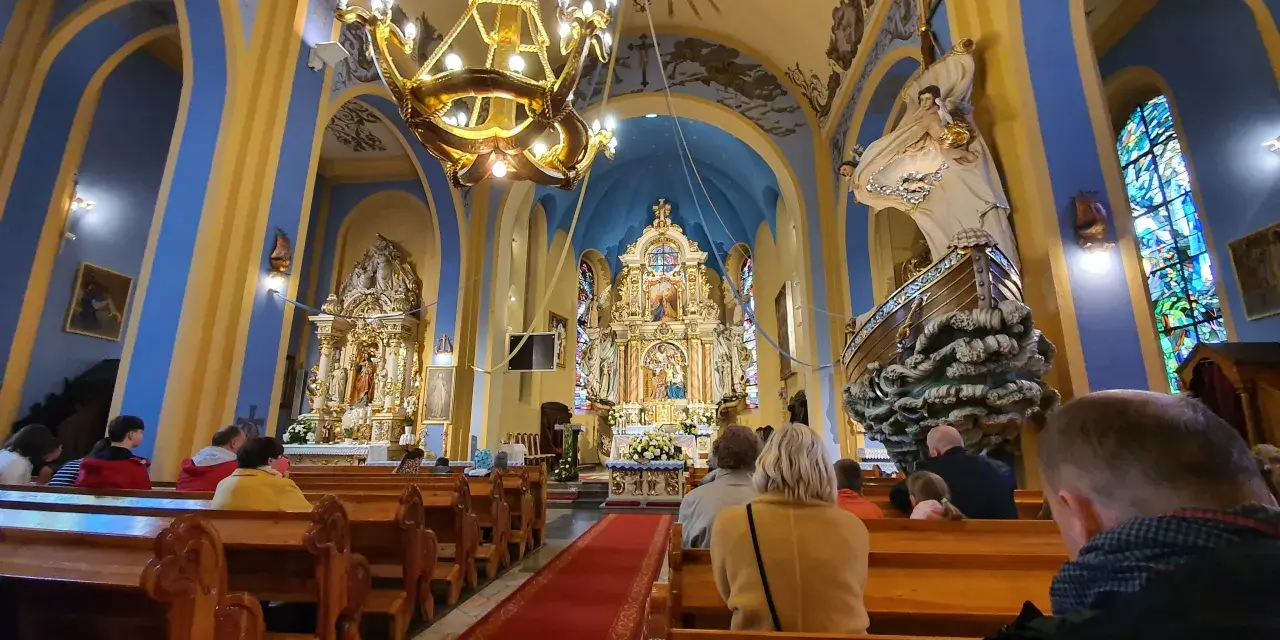Wnętrze kościoła w Jastarni z wiernymi na ławkach. Złoty ołtarz, błękitne ściany i ozdobny żyrandol tworzą uroczystą atmosferę.