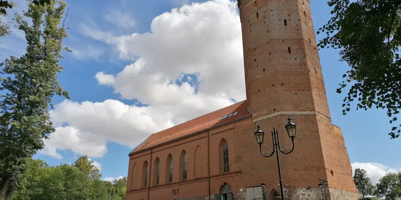 Zamek Człuchów, ceglana wieża i budynek muzeum pod błękitnym niebem z chmurami.
