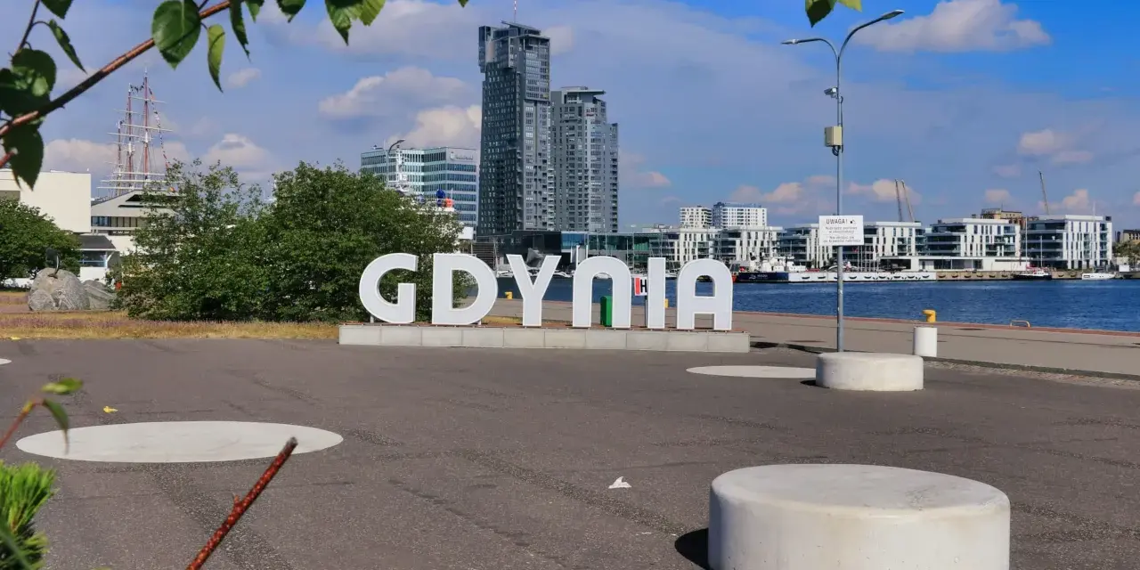 Napis GDYNIA na tle nowoczesnej architektury i żaglowca. Widok na port i budynki w Gdynia old town.