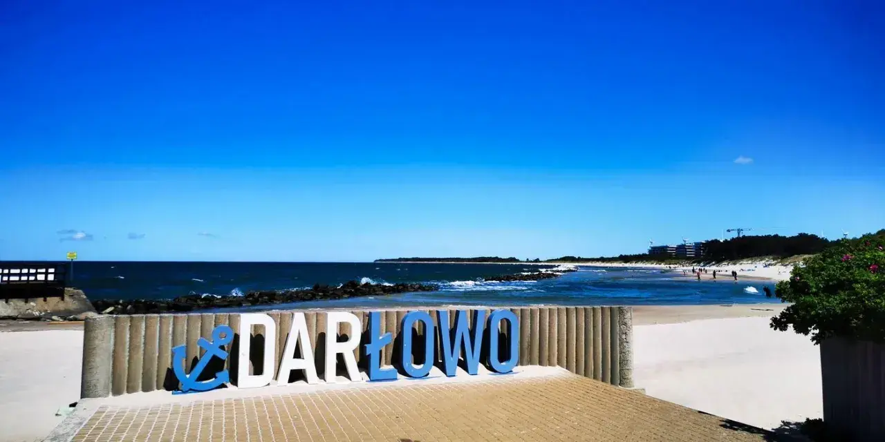 Napis "DARŁOWO" na tle plaży i morza. Darłówko zaprasza na wypoczynek nad Bałtykiem.