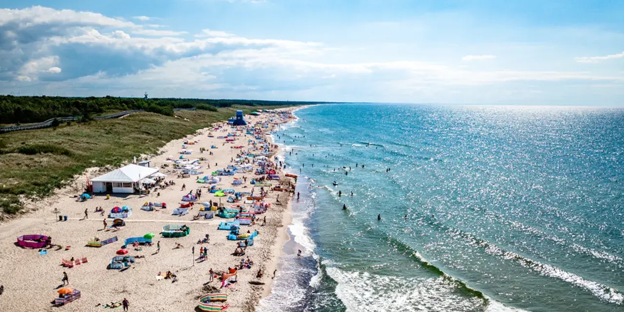 Słoneczna plaża w Darłówku pełna ludzi, kolorowych parawanów i namiotów. Woda w Bałtyku błyszczy, a fale zachęcają do kąpieli. To idealne miejsce na wakacyjne atrakcje.