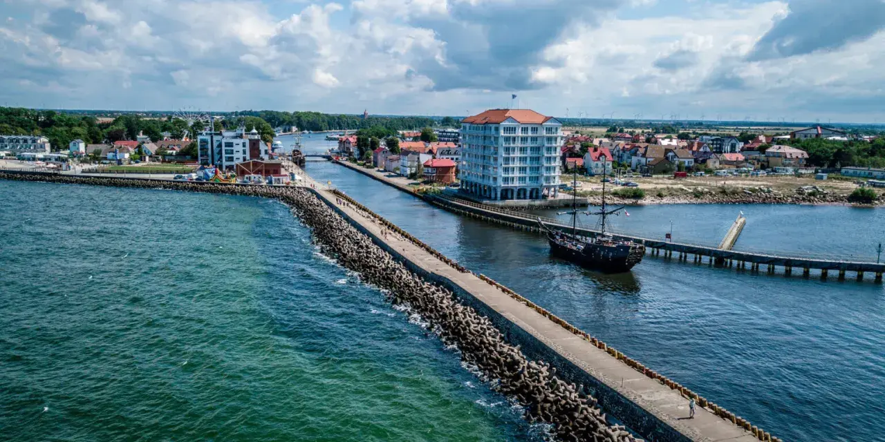 Widok na port w Darłówku Zachodnim z falochronem, budynkiem i statkiem pirackim.
