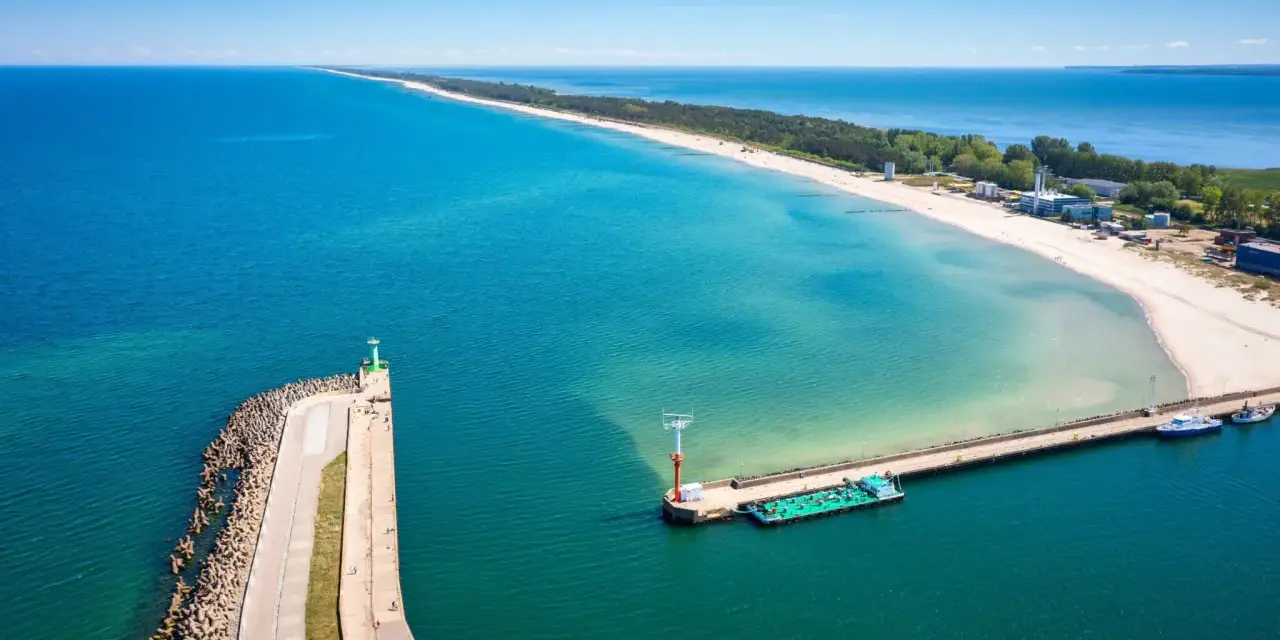 Władysławowo miasto, port z falochronem i latarnią morską, na tle piaszczystej plaży i turkusowego morza.