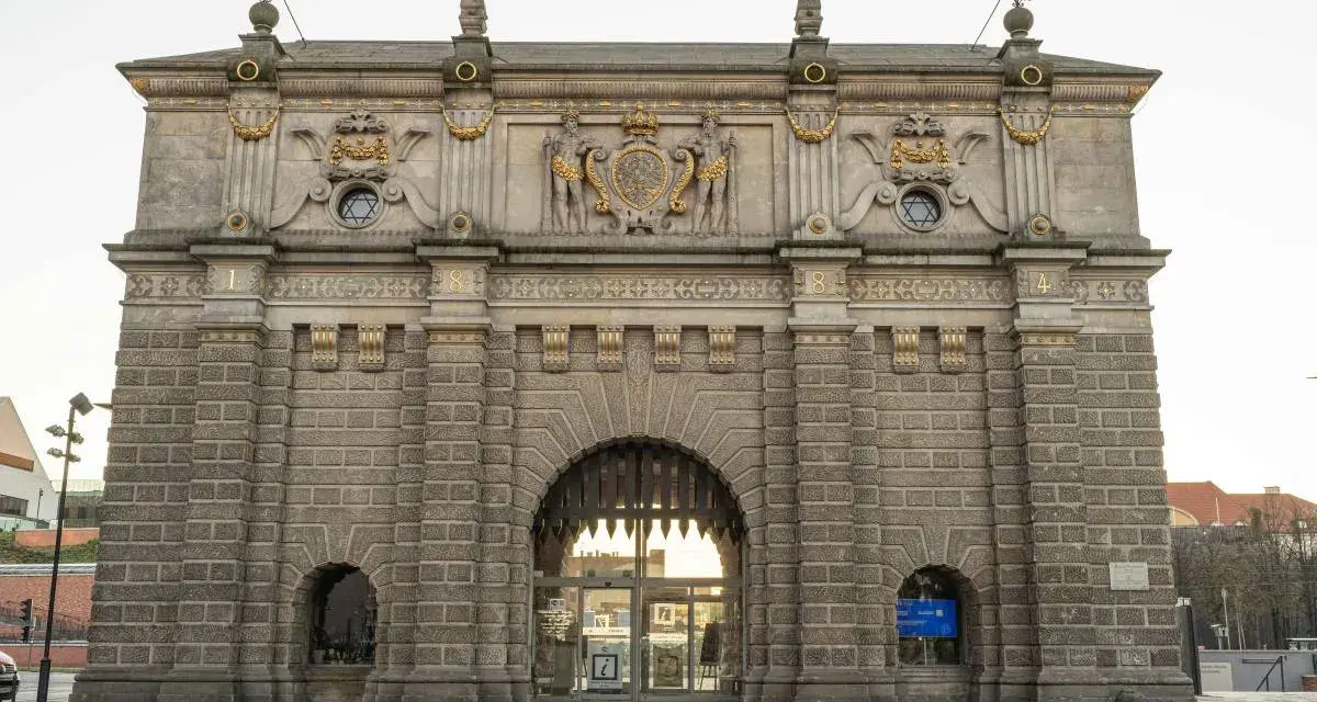 Majestatyczna Brama Wyżynna w Gdańsku, ozdobiona herbem i rzeźbami, zaprasza do zwiedzania.