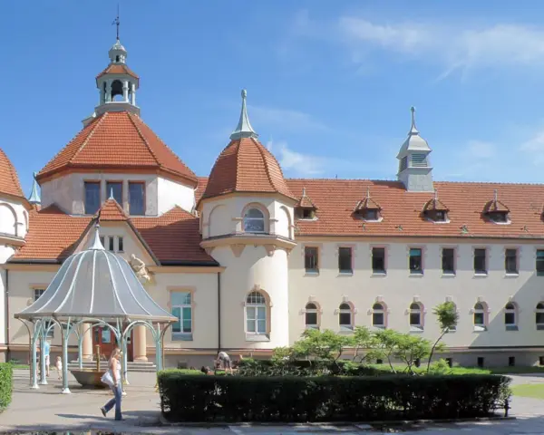 Elegancki zakład balneologiczny Sopot z charakterystycznymi wieżyczkami i czerwonym dachem, otoczony zielenią.