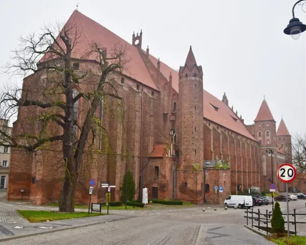 Imponująca katedra w Kwidzynie, z cegły, z charakterystycznymi wieżami i czerwonym dachem, otoczona drzewami i budynkami.
