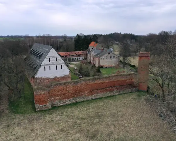 Zamek Kiszewski, z ceglanymi murami i wieżą, otoczony zielenią i drzewami.