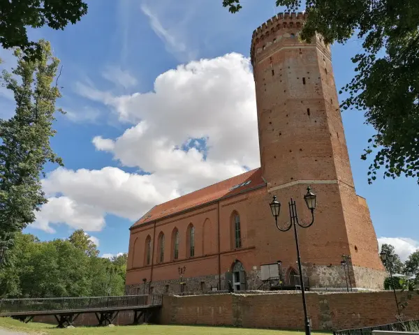 Zamek Człuchów, ceglana wieża i budynek muzeum pod błękitnym niebem z chmurami.