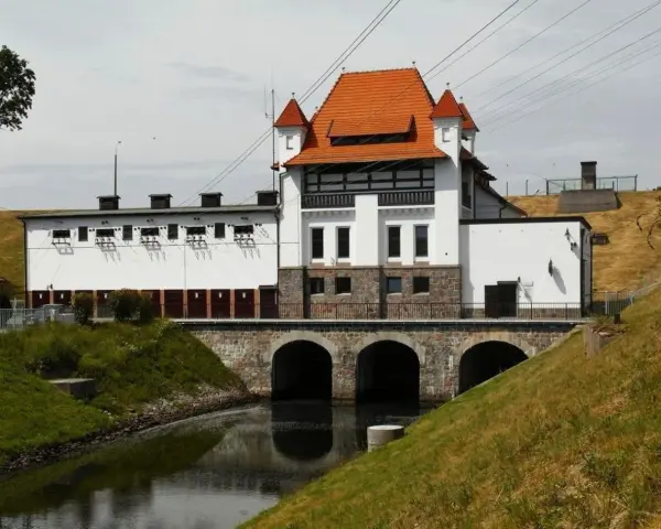 Elektrownia wodna Straszyn z charakterystycznym czerwonym dachem i kamiennymi arkadami nad kanałem.