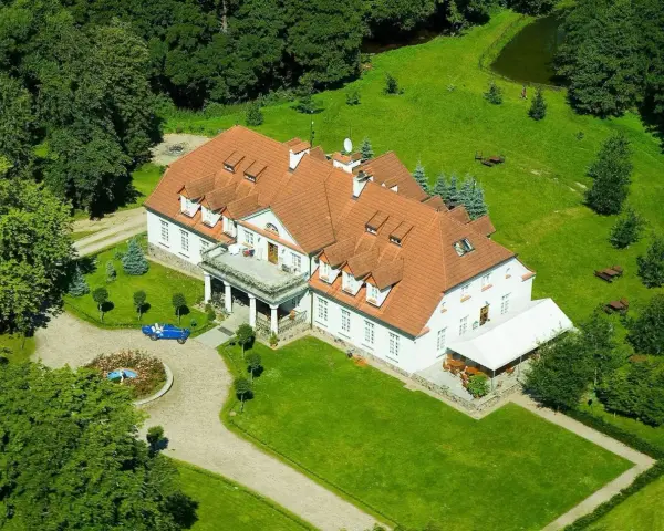 Dwór w Bychowie otoczony zielenią, z niebieskim kabrioletem przy różanym klombie.