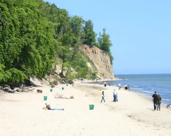 Słoneczny dzień na plaży przy klifie orłowskim. Ludzie spacerują, odpoczywają, a morze spokojnie faluje.