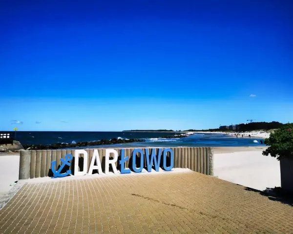 Napis "DARŁOWO" na tle plaży i morza. Darłówko zaprasza na wypoczynek nad Bałtykiem.