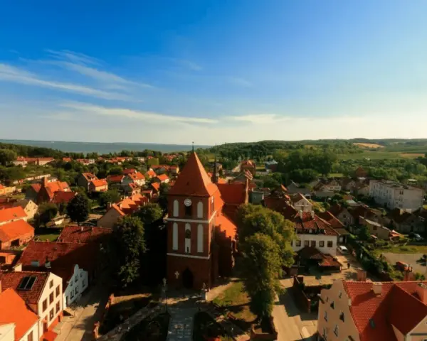 Widok na urokliwe Tolkmicko z charakterystyczną wieżą kościelną. Wśród czerwonych dachów i zieleni rozciąga się malowniczy krajobraz, idealny na odkrywanie tolkmickich atrakcji.