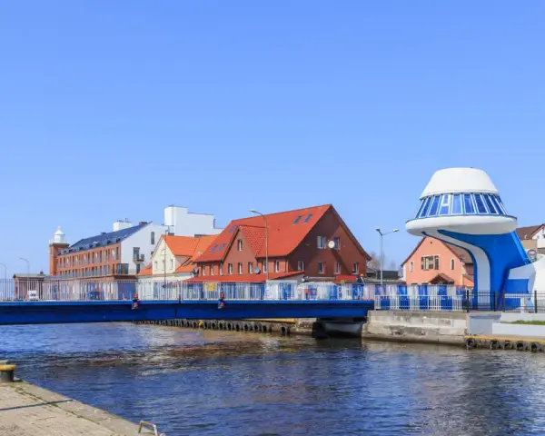 Port rybacki nad Wieprzą z niebieskim mostem i charakterystycznym budynkiem w kształcie statku kosmicznego.