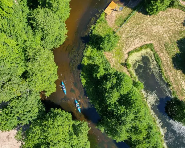 Dwie kajaki płyną rzeką pośród zieleni. To wspaniałe **Kociewie atrakcje** dla miłośników przyrody i aktywnego wypoczynku.